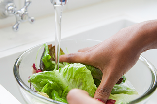 Hand wäscht Salat in Glasschüssel über Waschbecken