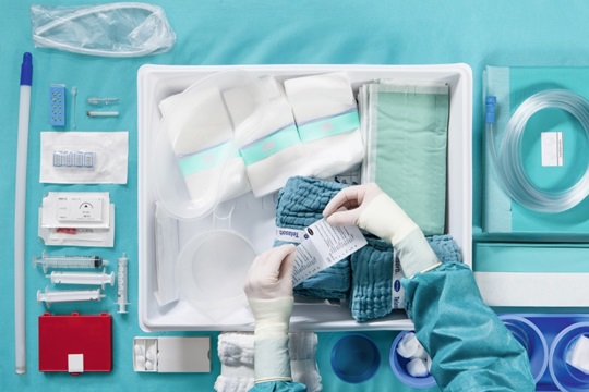 The picture shows an operation table, where all surgical instruments are lined up. Two hands in sterile gloves are over the table, holding a piece of paper.