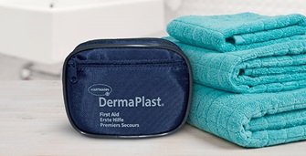 Hartmann DermaPlast® first aid kit and turquoise blue towels stacked in bathroom in front of sink.